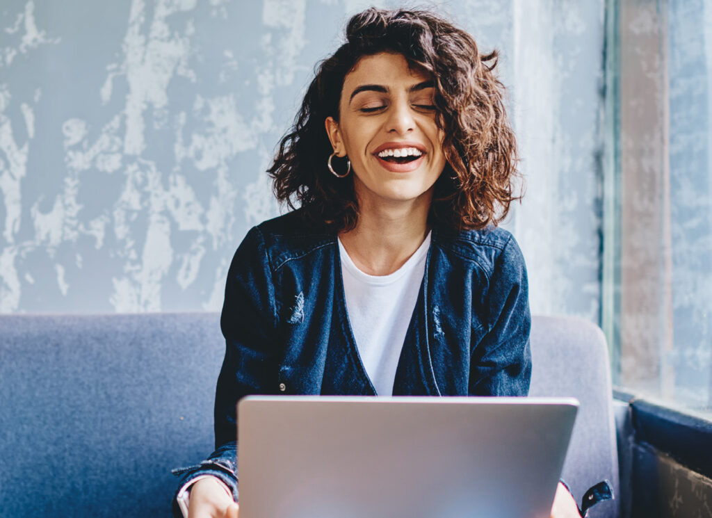 Happy stylish female laughing while on laptop device