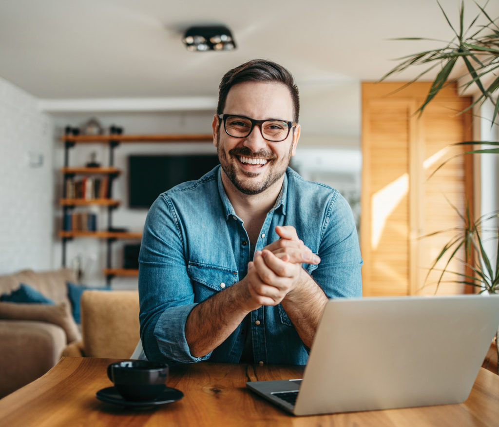 Happy guy smiling at camera with computer in front of him