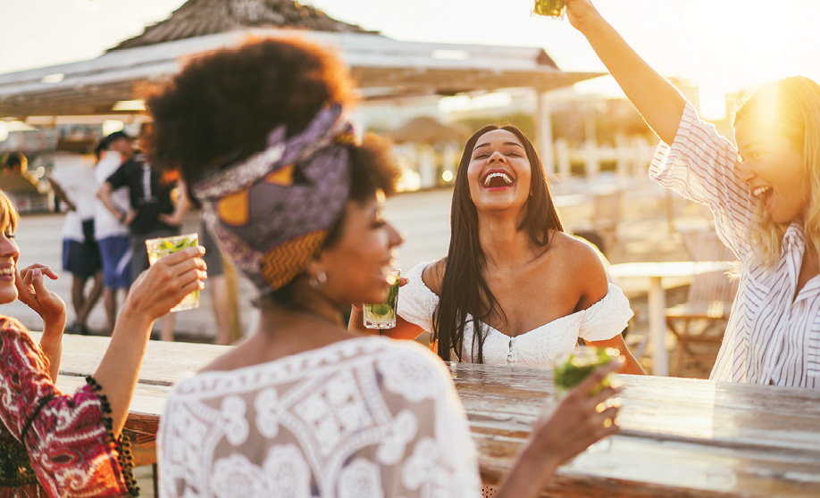 Happy girls having fun drinking cocktails at bar on the beach