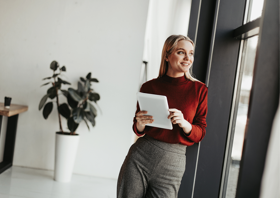 Cheerful happy young blonde woman stand in office room and lean to window